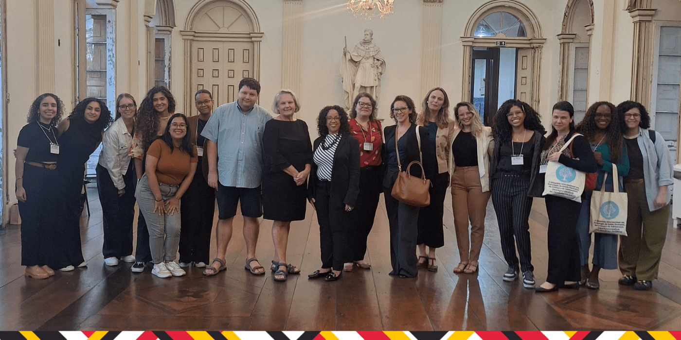 A group of students and faculty stand together in a historic building with tall doors and wooden floors.