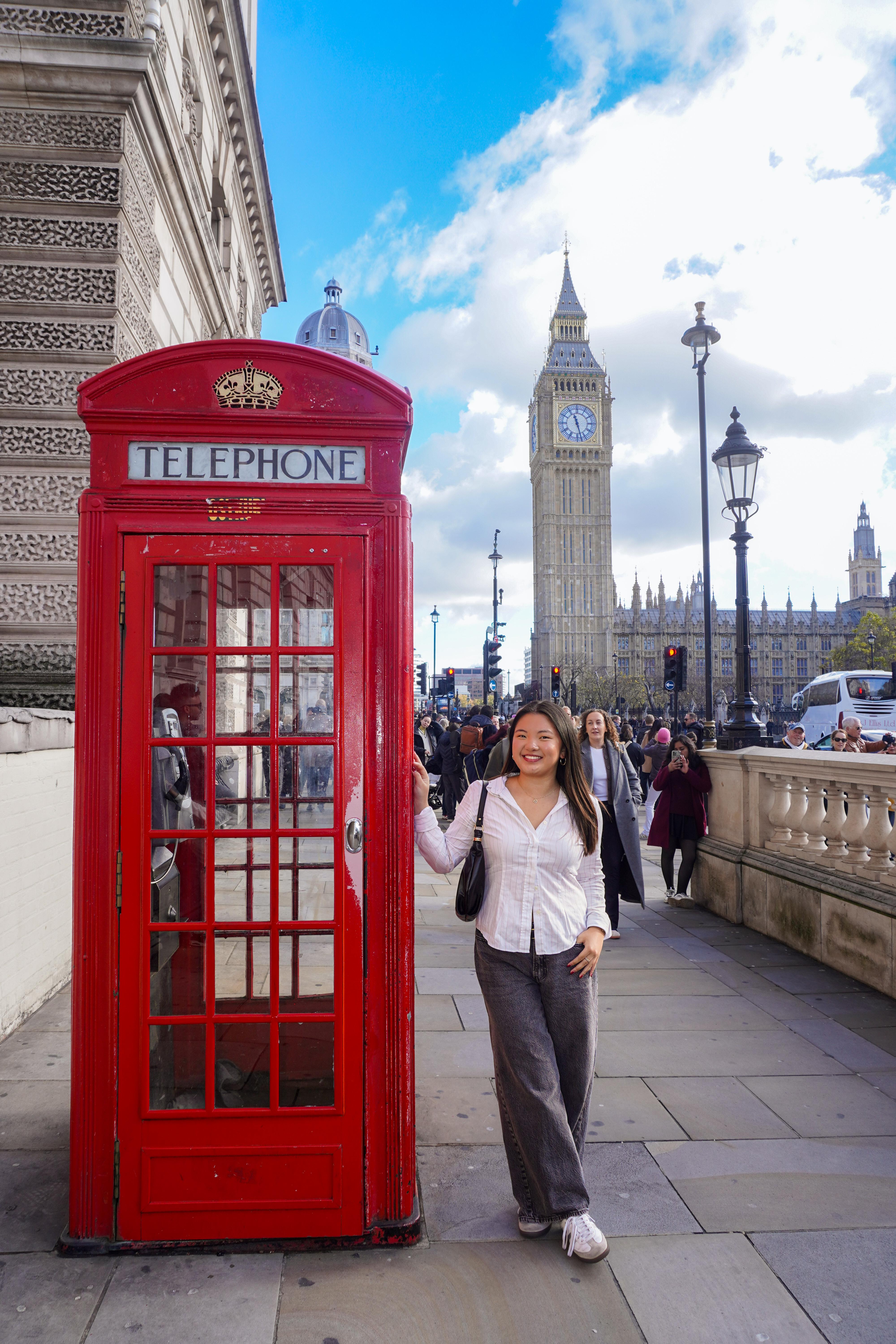 Eileen stands next to an large red phone booth with London's Big Ben clocktower in the background.