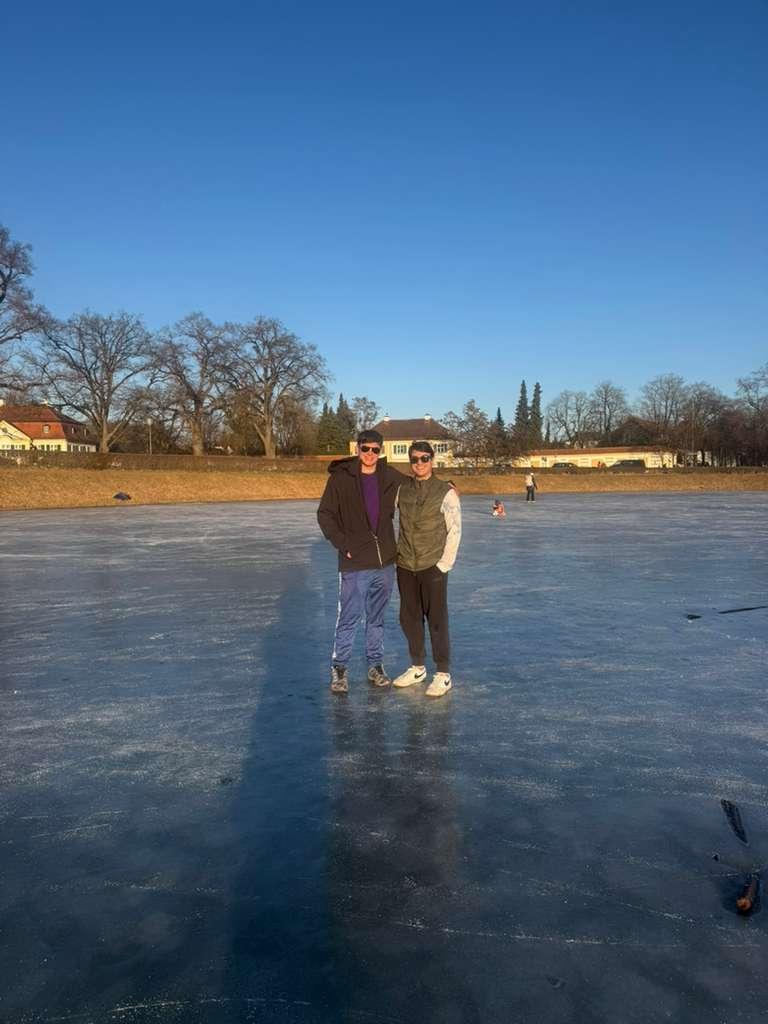 Two students stand on a frozen lake under a blue sky.