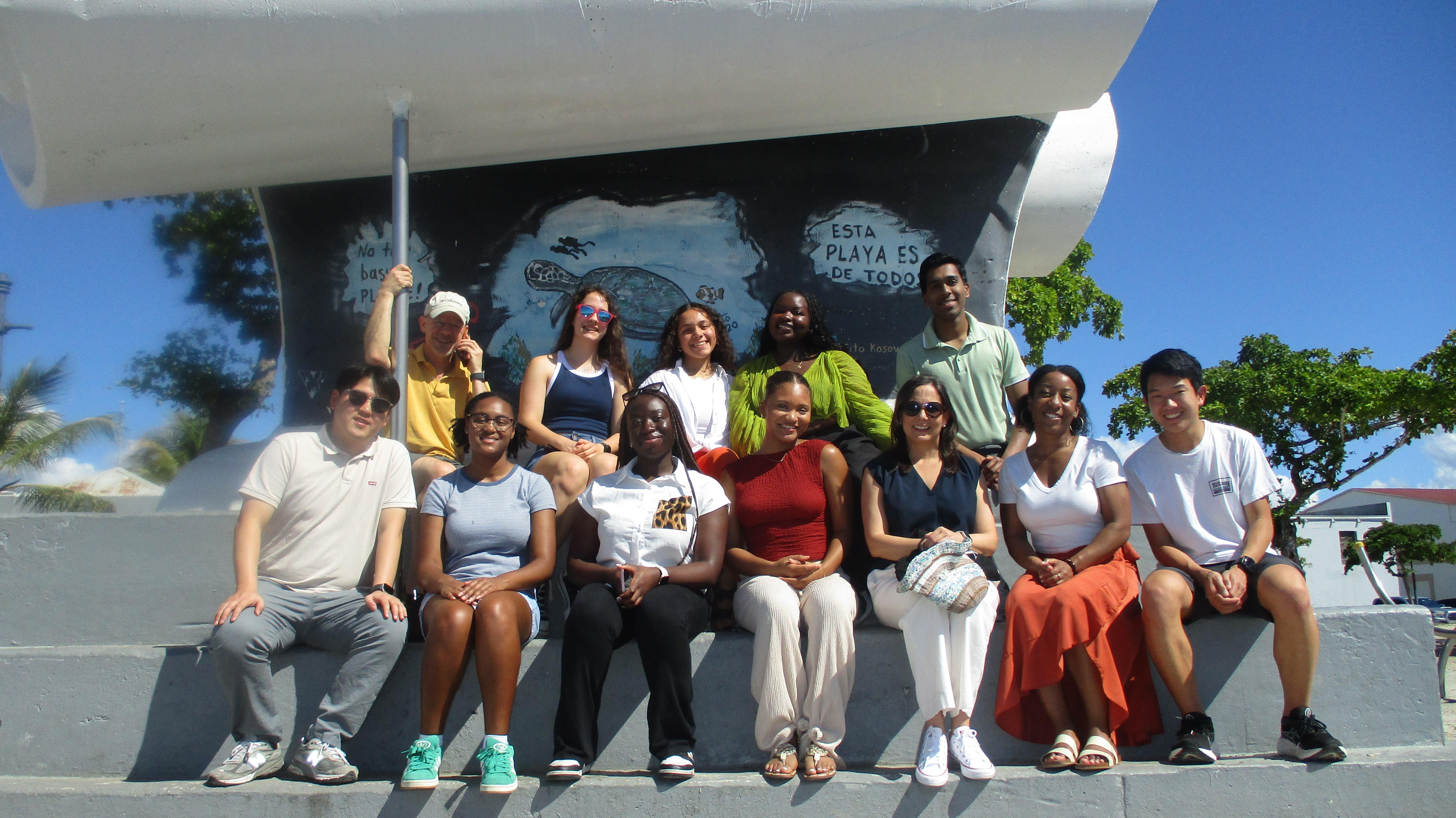 Group seated on steps in front of mural