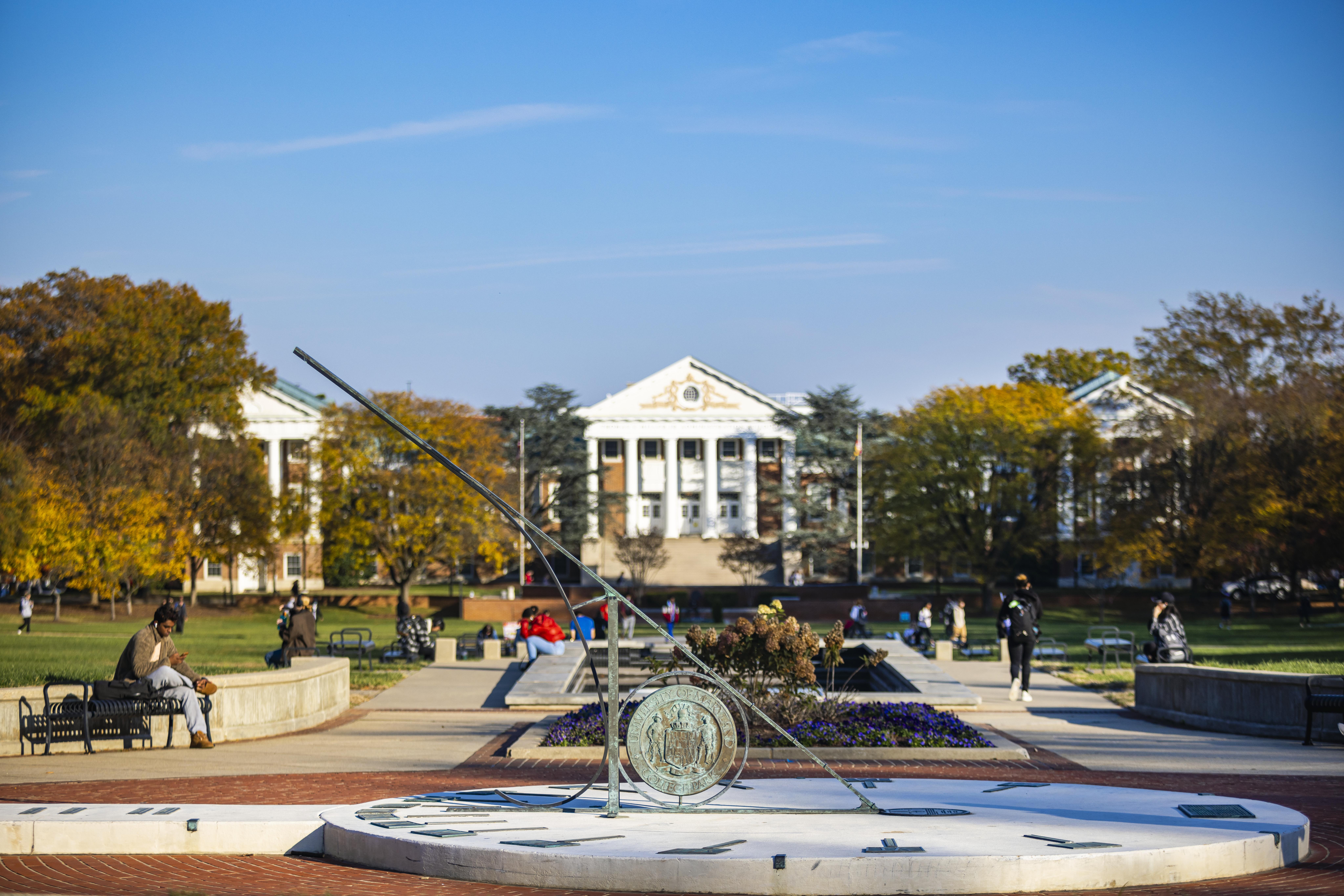 Photo of the UMD Sundial and Administration Building with students resting on benches lining the fountain.
